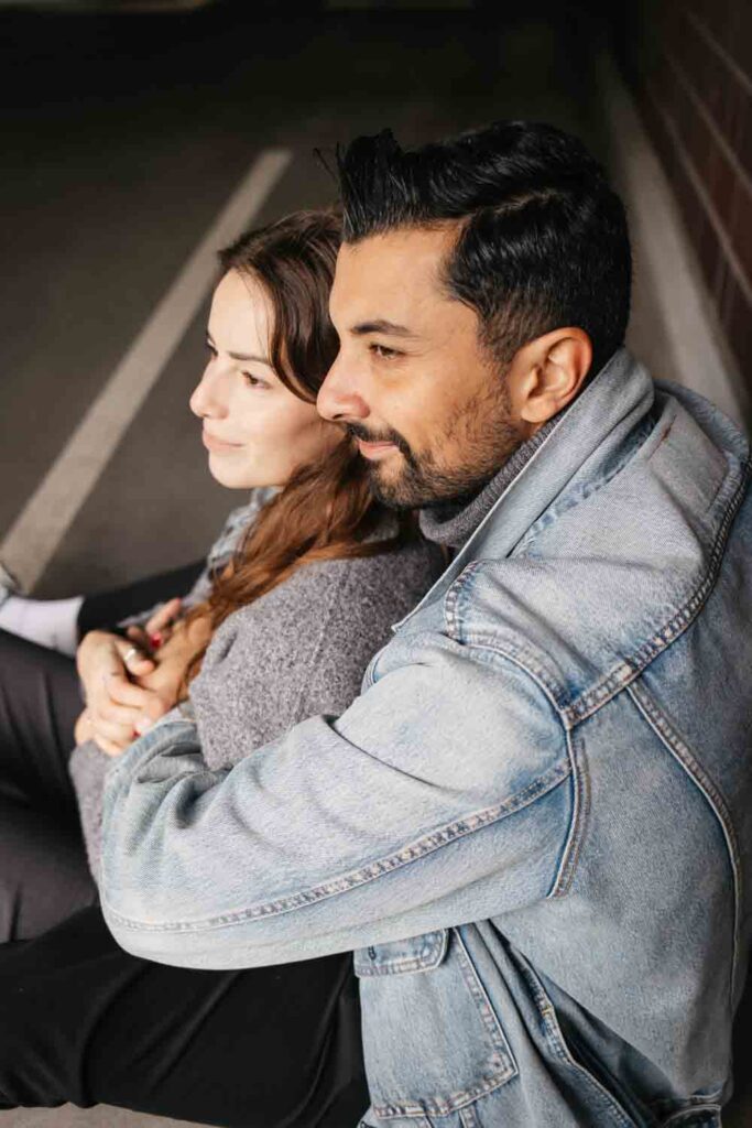 Paarshooting Dortmund auf dem Parkdeck Paar sitzt voreinander und schaut in die Ferne, er umarmt sie von hinten