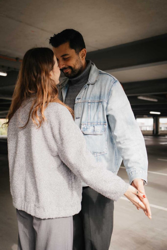 Paarshooting Dortmund auf dem Parkdeck Paar steht zueinander ganz eng zusammen und ihre Hände berühren sich leicht, beide lächeln