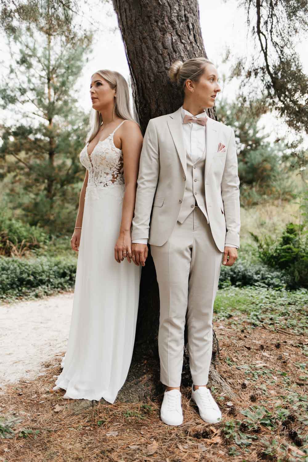 Hochzeitspaar lehnt am Baum, die kleinen Finger halten sich, sie schauen in unterschiedliche Richtungen