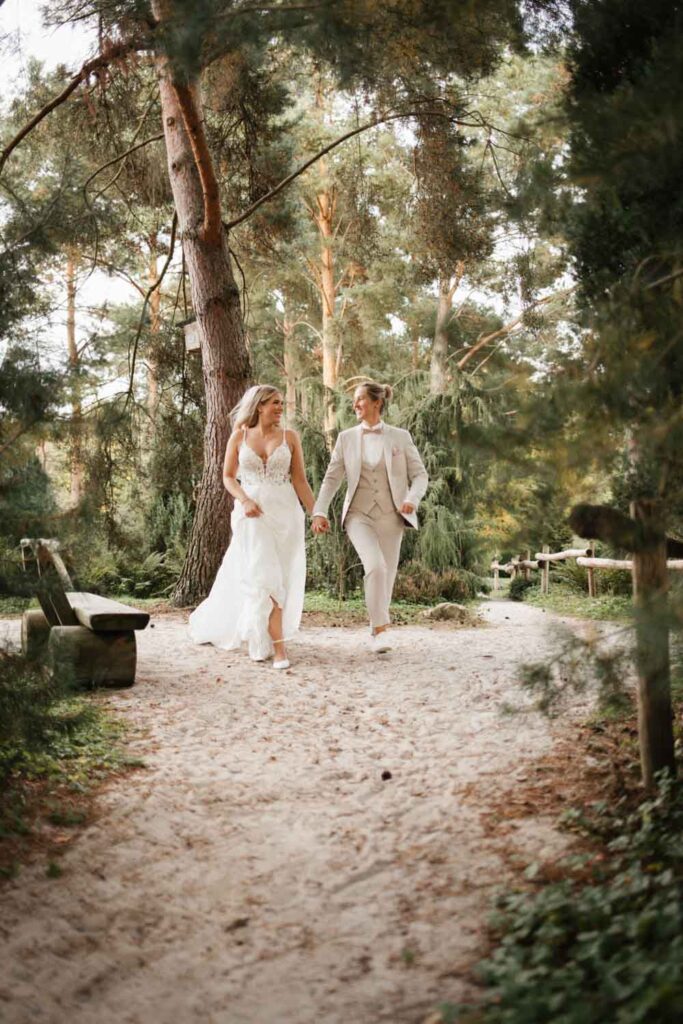 Hochzeitspaar rennt im Sand auf die Kamera zu und schasut sich an