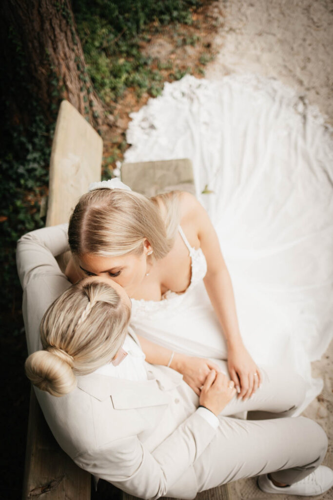 Hochzeitspaar sitzt auf der Bank und küsst sich.