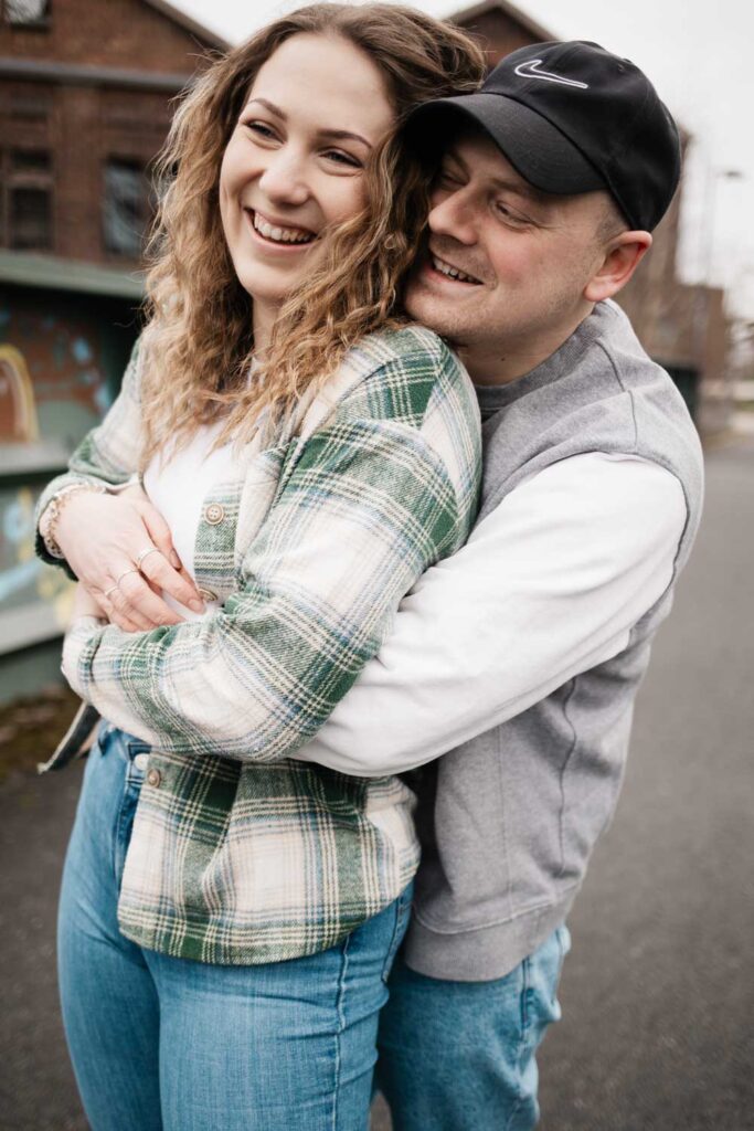 Paarshooting Phoenix West Dortmund Freund umarmt Freundin von hinten, beide lachen