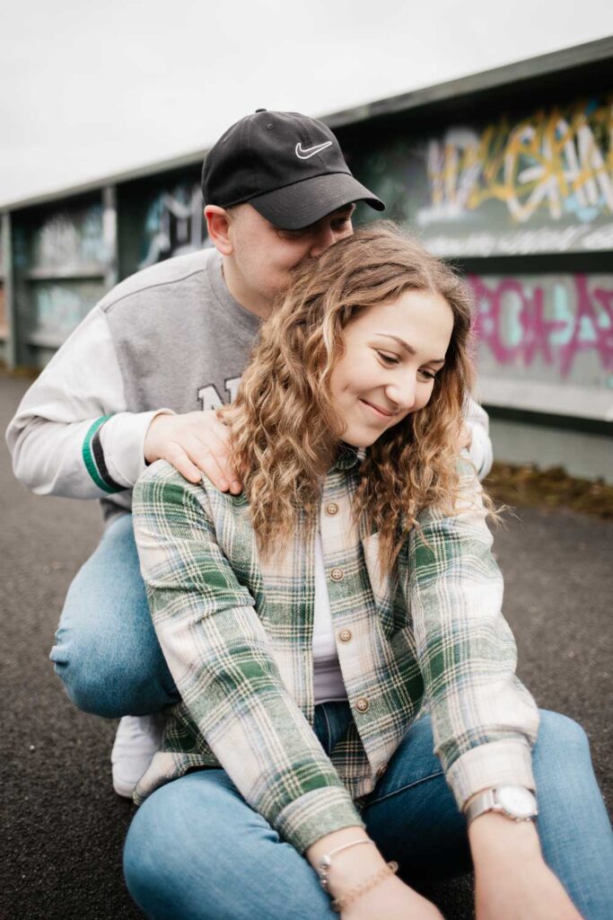 Paarshooting Phoenix West Freundin sitzt auf dem Boden, Freund hockt hinter ihr und küsst ihren Kopf