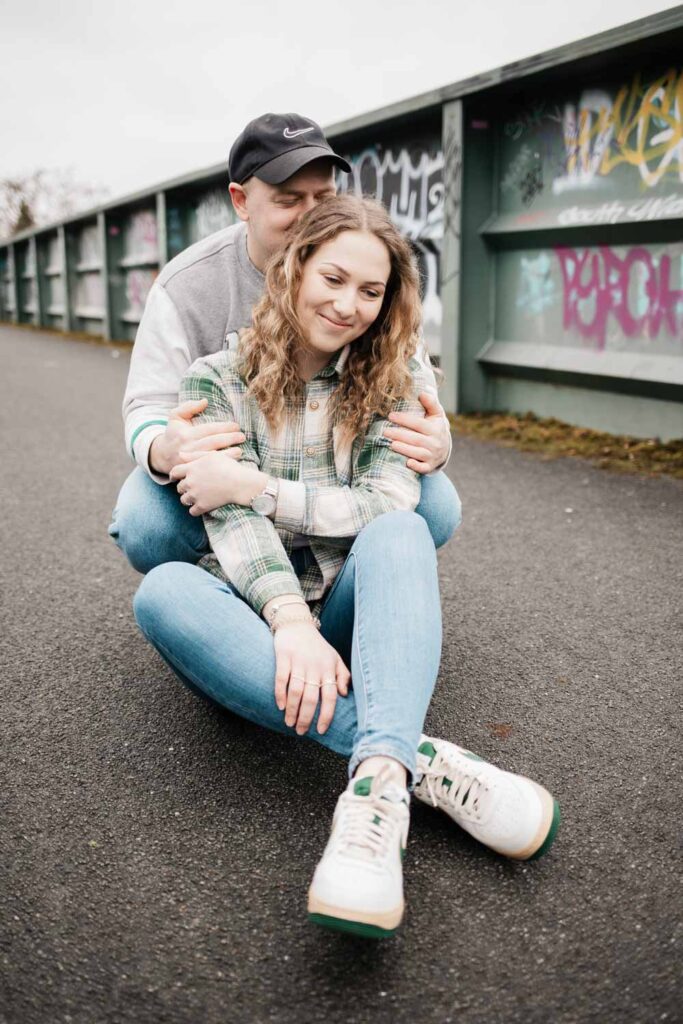 Paarshooting Phoenix West Freundin sitzt auf dem Boden, Freund hockt hinter ihr und küsst ihren Kopf er hat die Augen zu