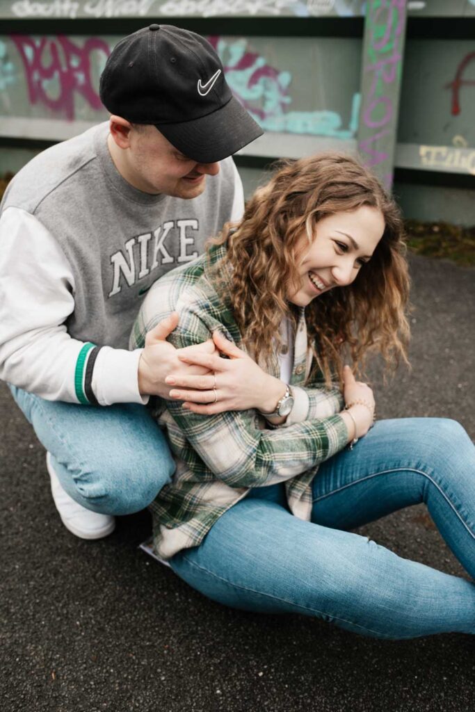 Paarshooting Phoenix West Freundin sitzt auf dem Boden, Freund hockt hinter ihr und beide lachen