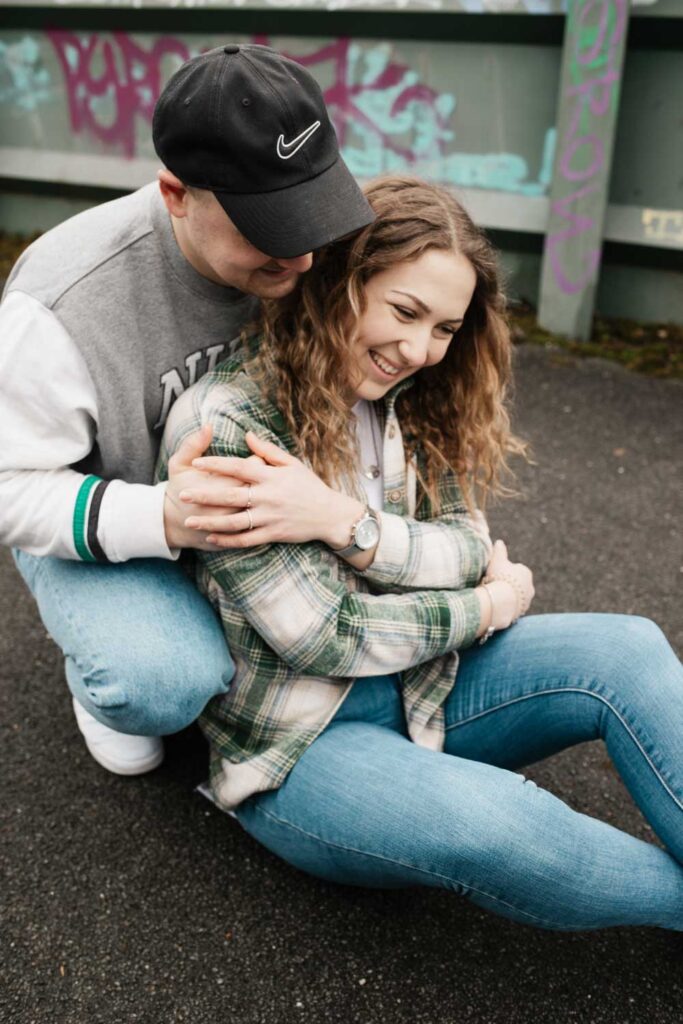 Paarshooting Phoenix West Freundin sitzt auf dem Boden, Freund hockt hinter ihr und beide lächeln doll