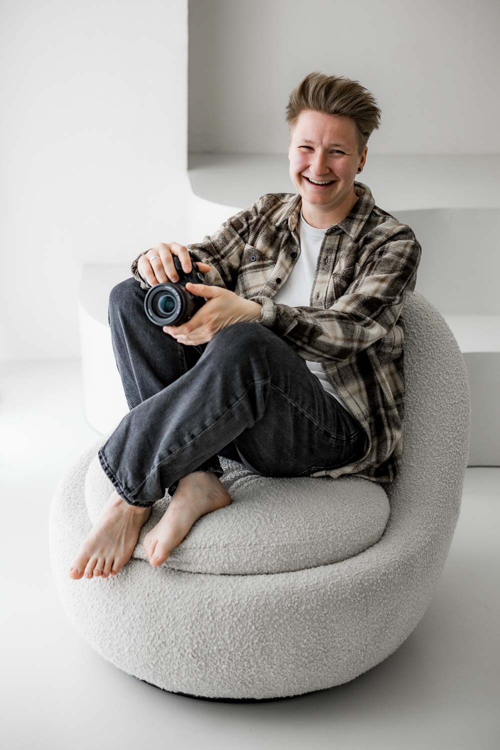 Hochzeitsfotografin sitzt lässig auf einem Sessel und lächelt in die Kamera
